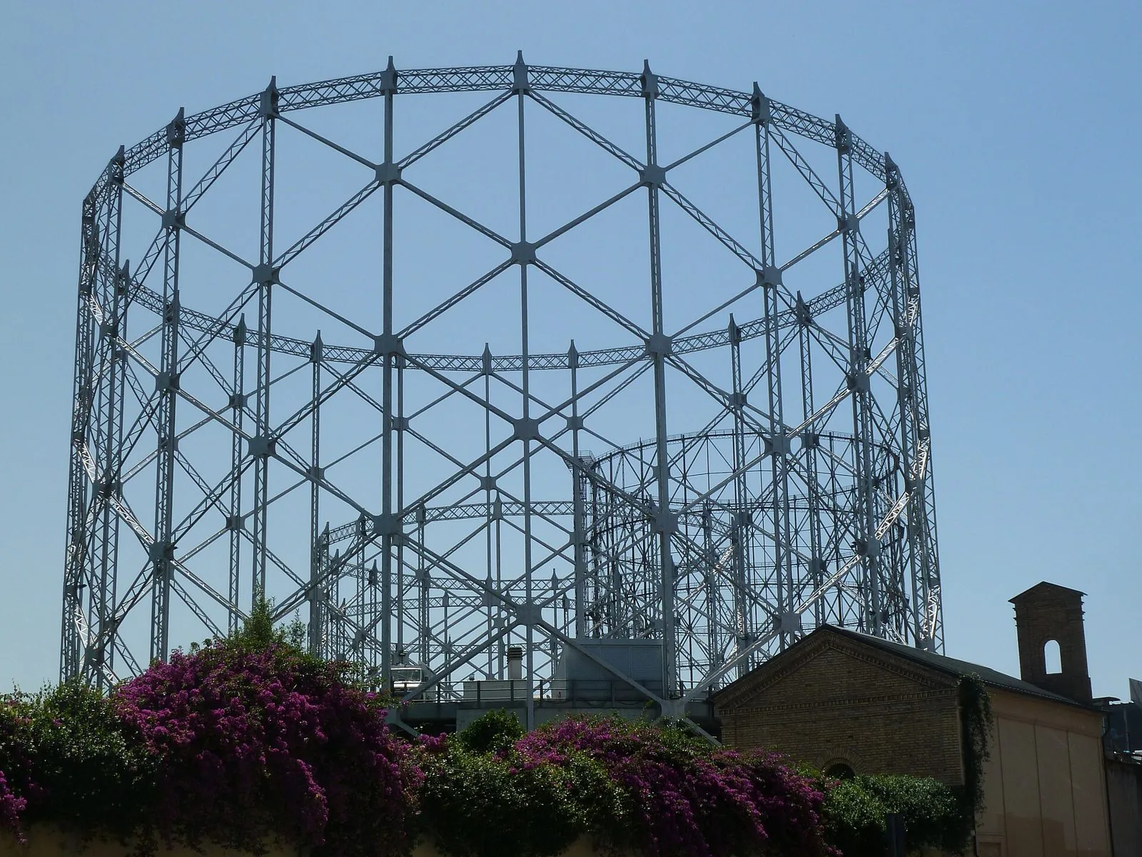 La struttura in acciaio del Gazometro di via Ostiense contro il cielo azzurro, con bouganville in fiore