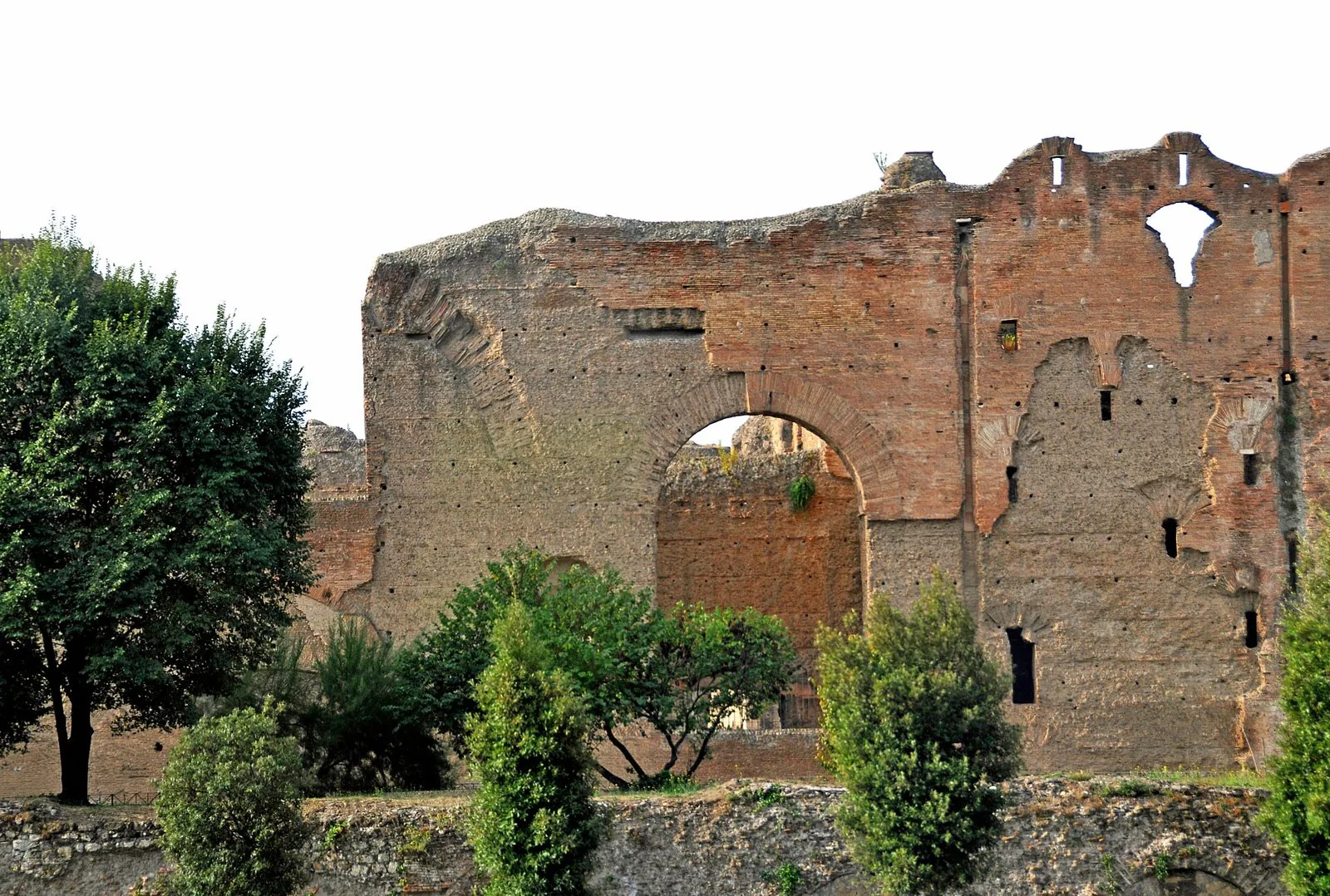 I grandi muri in laterizio delle Terme di Caracalla con un arco aperto e alberi in primo piano